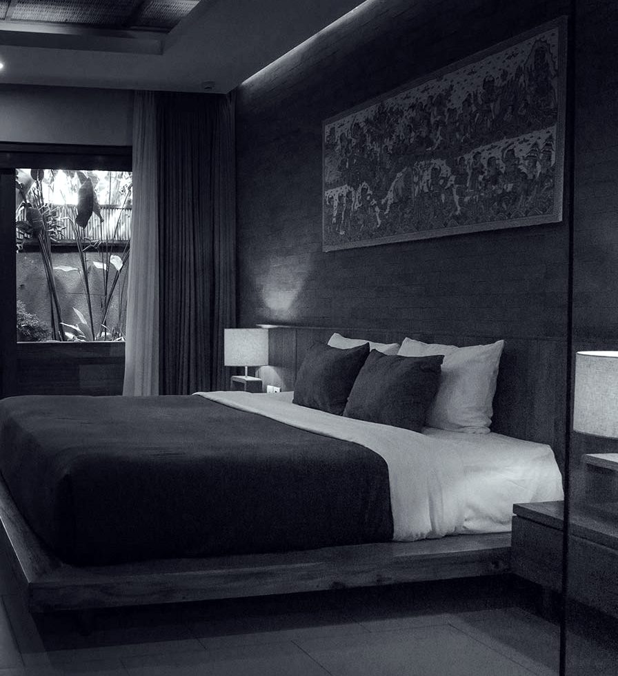 A dark room with a desk, a robe hanging and the bed against a panelled wall